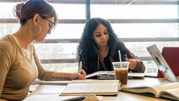 Math students working together at a table with notebooks, laptop, coffee